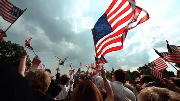 A crowd of people standing outside on a cloudy day, waving the American Flag in support of democracy.